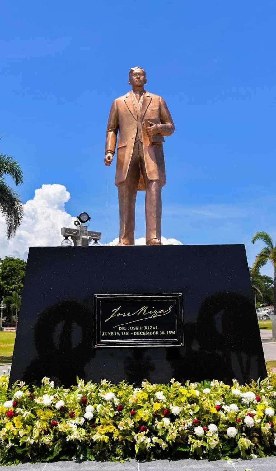 Bronze statue of Dr. José Rizal at Rizal Boulevard Dumaguete with engraved plaque and tropical garden under blue sky