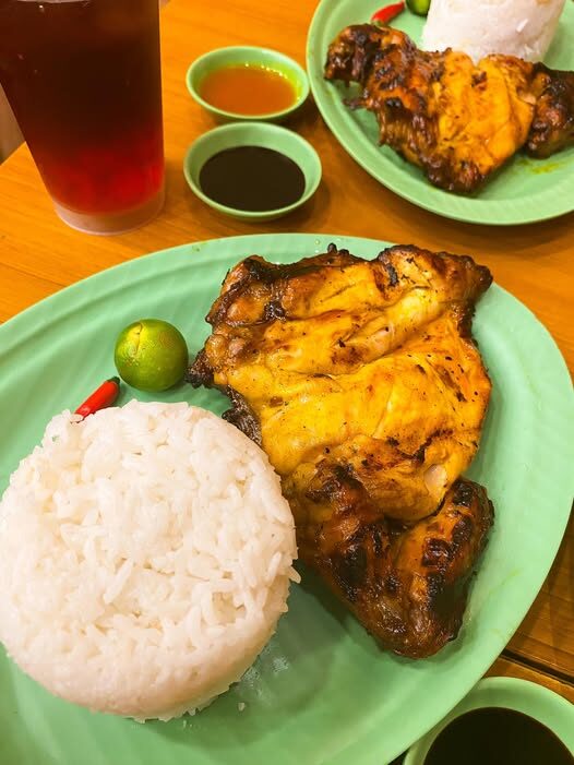 Authentic Bacolod chicken inasal grilled to bright orange-yellow color served on green karinderya plate with white rice, calamansi, red chili, and soy-vinegar dipping sauces