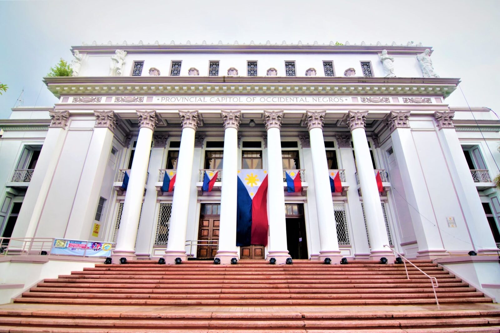 Bacolod Provincial Capitol of Occidental Negros neoclassical white building with Corinthian columns and Philippine flags draped on facade