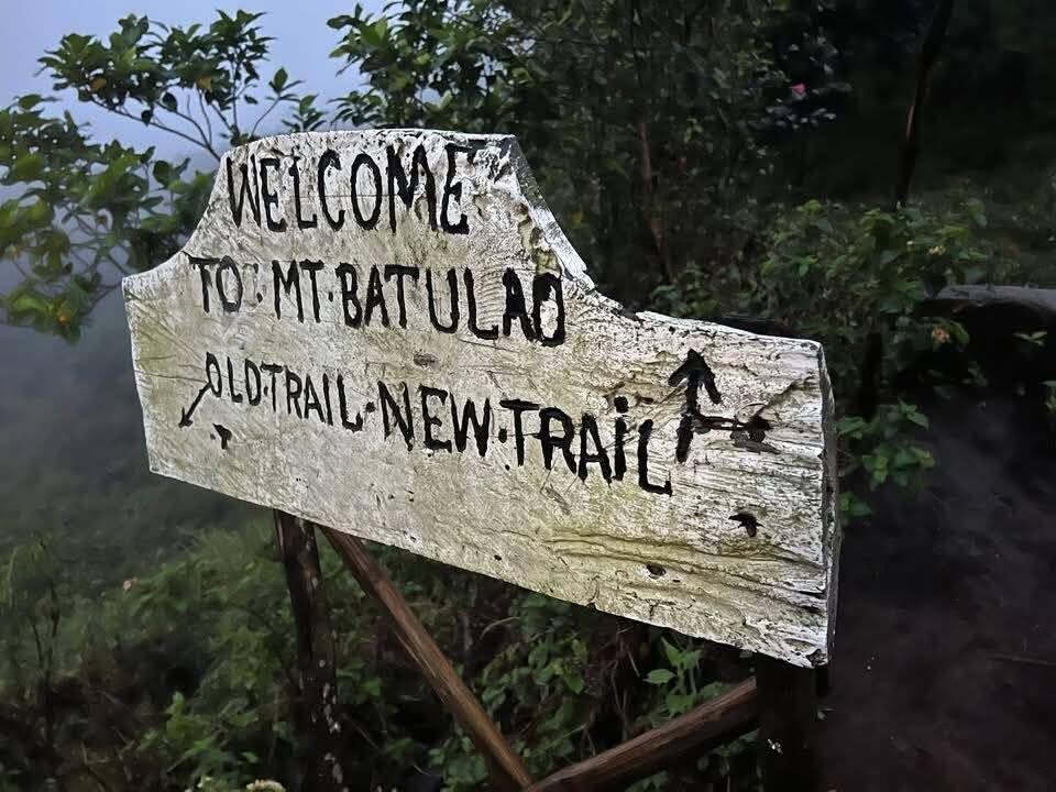 Mt. Batulao Batangas weathered wooden trail sign welcoming hikers with arrows pointing to Old Trail and New Trail at misty mountain trailhead