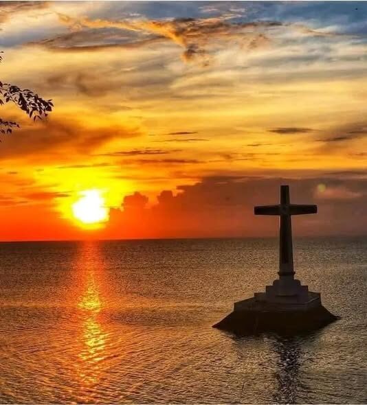 Camiguin Sunken Cemetery white cross silhouetted against golden sunset over the sea
