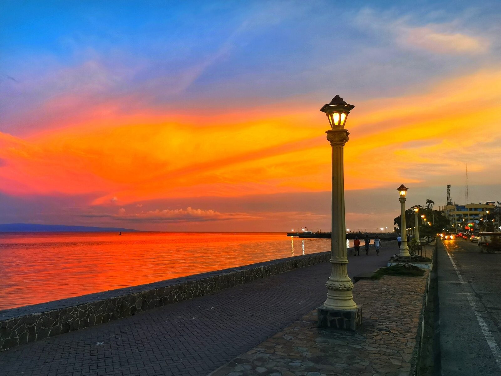 Rizal Boulevard Dumaguete dramatic orange sunset over the sea with iconic vintage street lamps and brick promenade