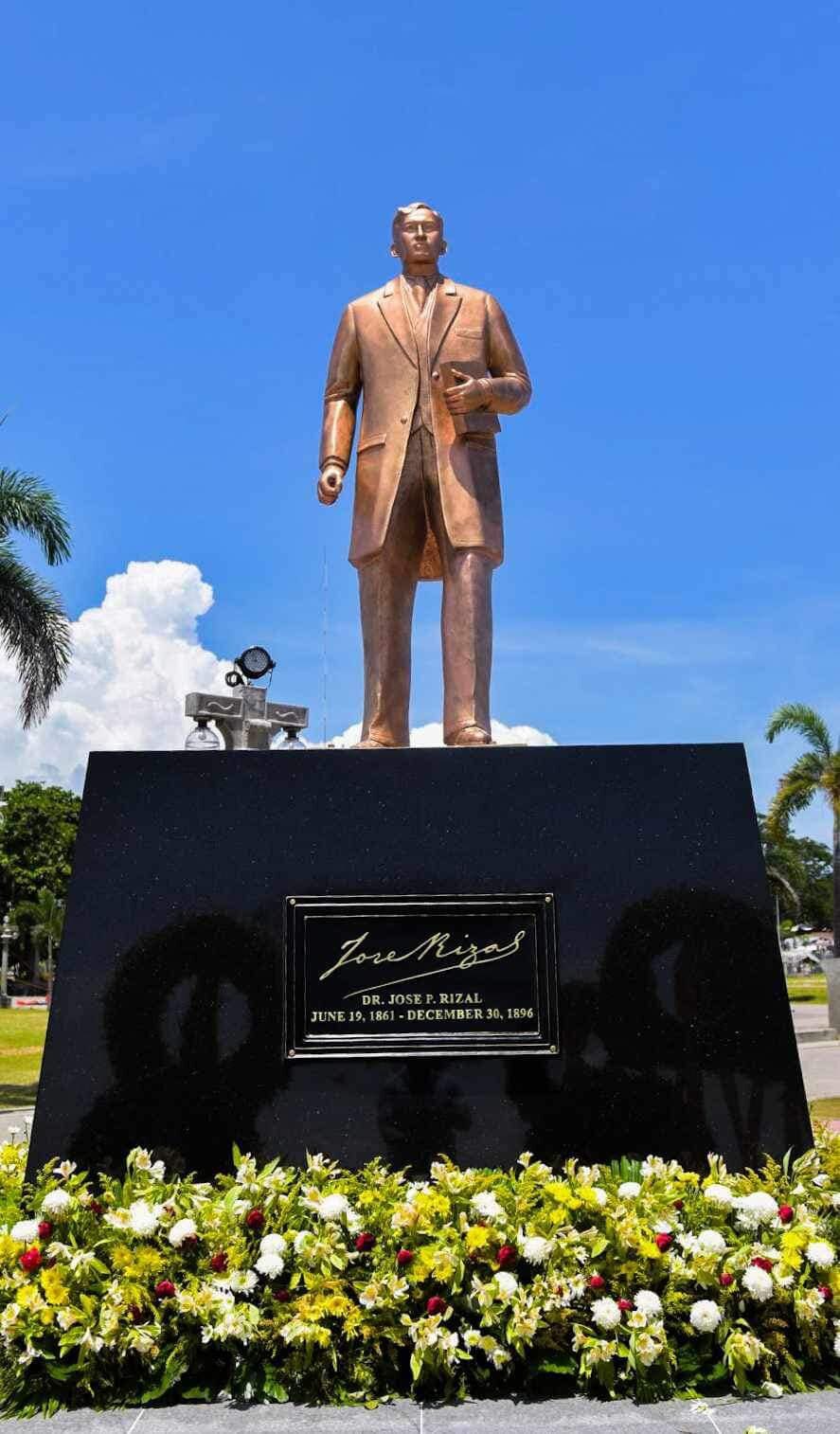 Bronze statue of Dr. José Rizal at Rizal Boulevard Dumaguete with engraved plaque and tropical garden under blue sky