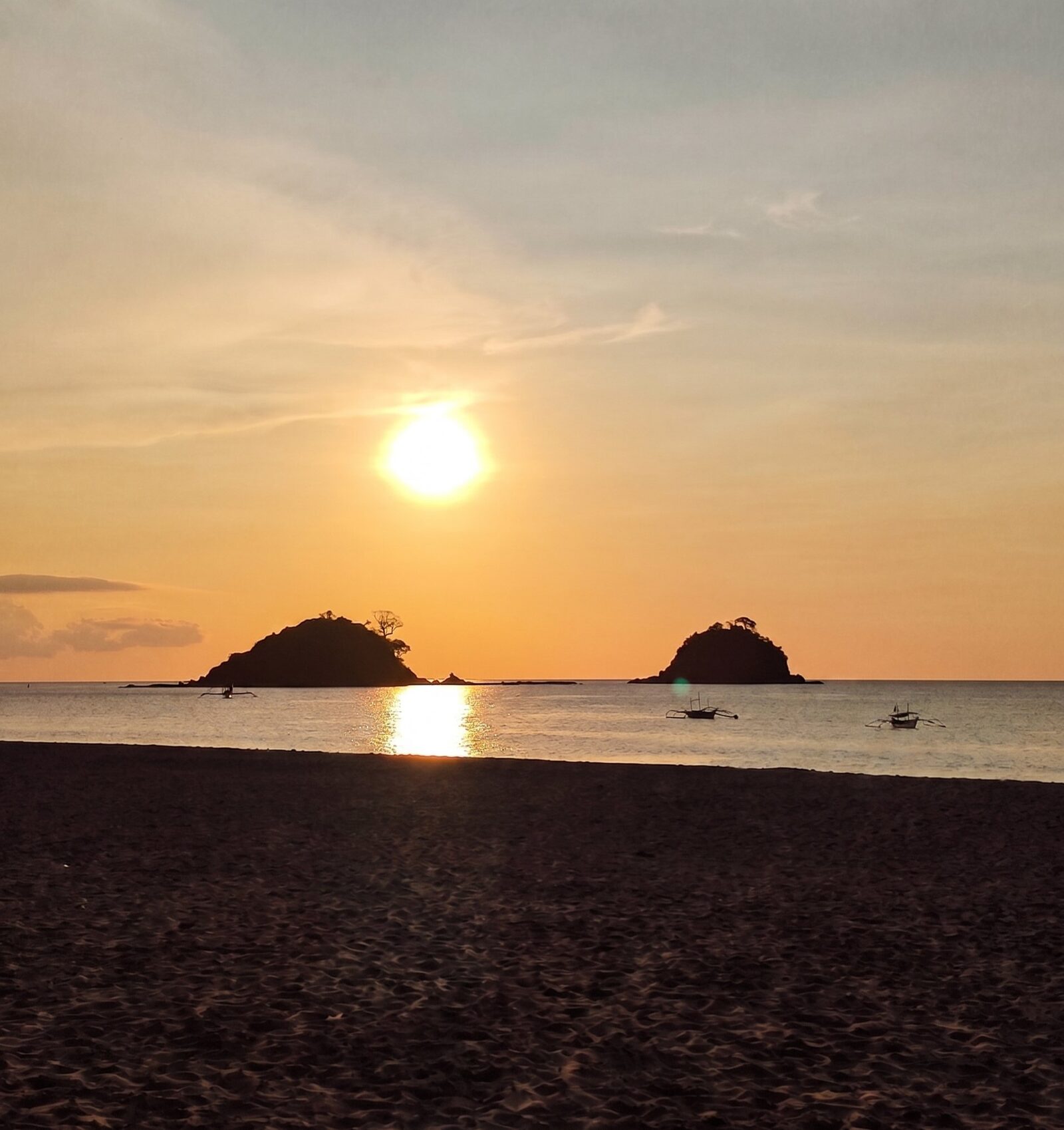 Sunset over Nacpan Beach El Nido with twin islands silhouetted on the horizon and outrigger boats in the calm water