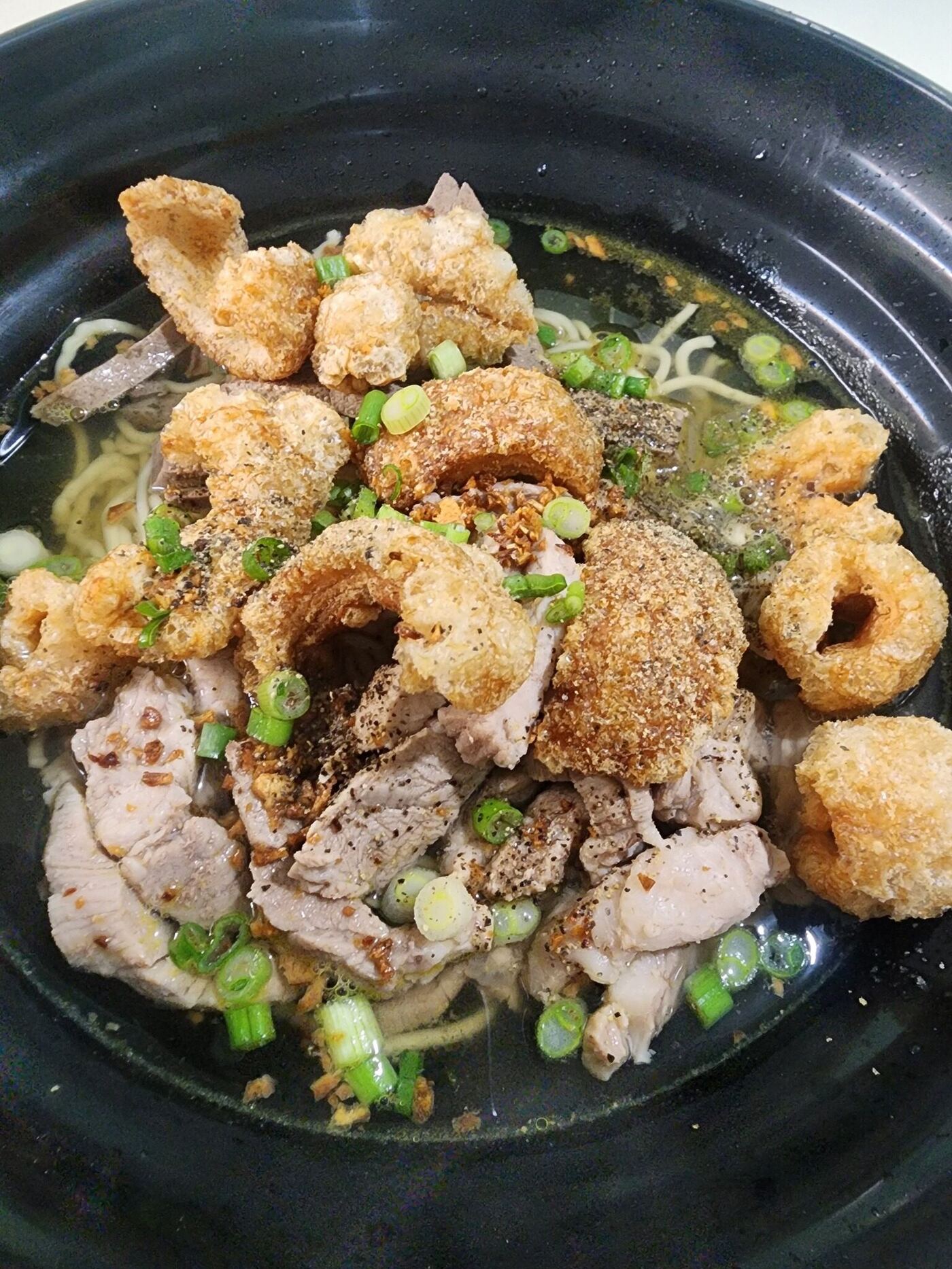 Authentic La Paz Batchoy Iloilo signature noodle soup with crispy chicharon, sliced pork, scallions, and rich pork bone broth in black bowl