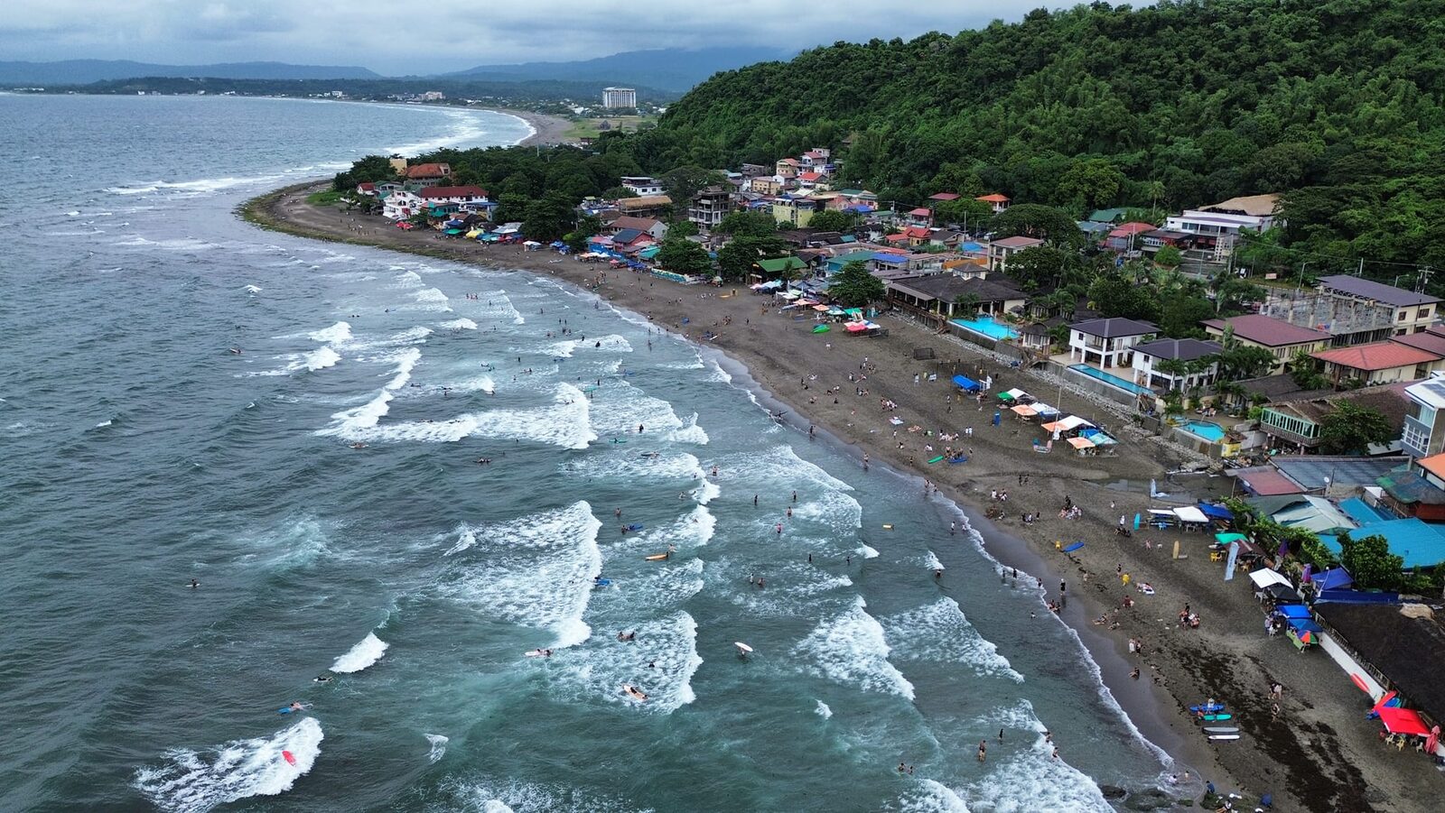 Aerial view of Urbiztondo Beach La Union surfers in the waves and resorts along the curving coastline