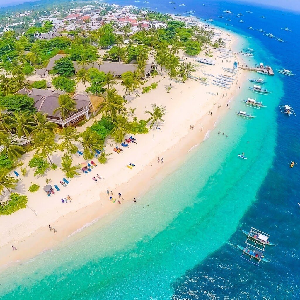 Aerial of Bounty Beach Malapascua Cebu palm-lined white sand beach with beach loungers, resorts, and dive boats in clear turquoise water