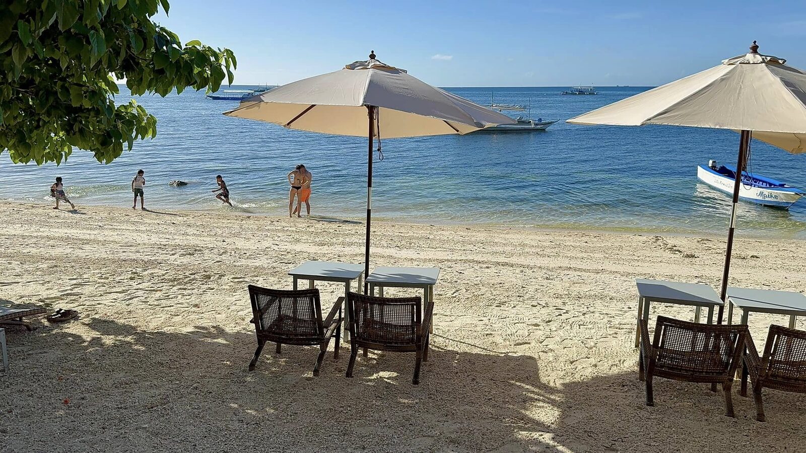 Bounty Beach Malapascua Cebu sandy beach scene with umbrellas, beach chairs, kids playing in shallow turquoise water, and bangka boats moored offshore