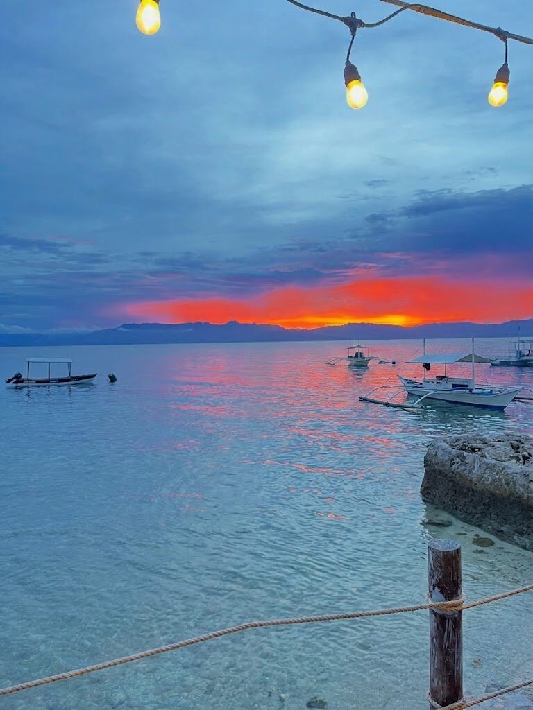 Sunset over Moalboal Cebu with bangka boats silhouetted on calm water and string lights overhead