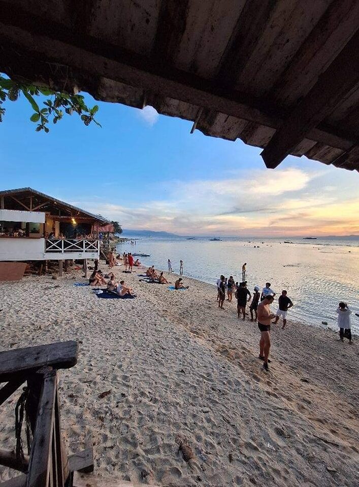 Panagsama Beach Moalboal Cebu sunset scene with beachfront restaurant deck and bangka boats on calm water
